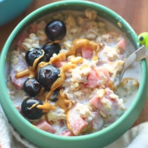 Close up of a bowl of strawberry overnight oats topped with blueberries.