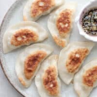 pan fried dumplings on a plate with dipping sauce.