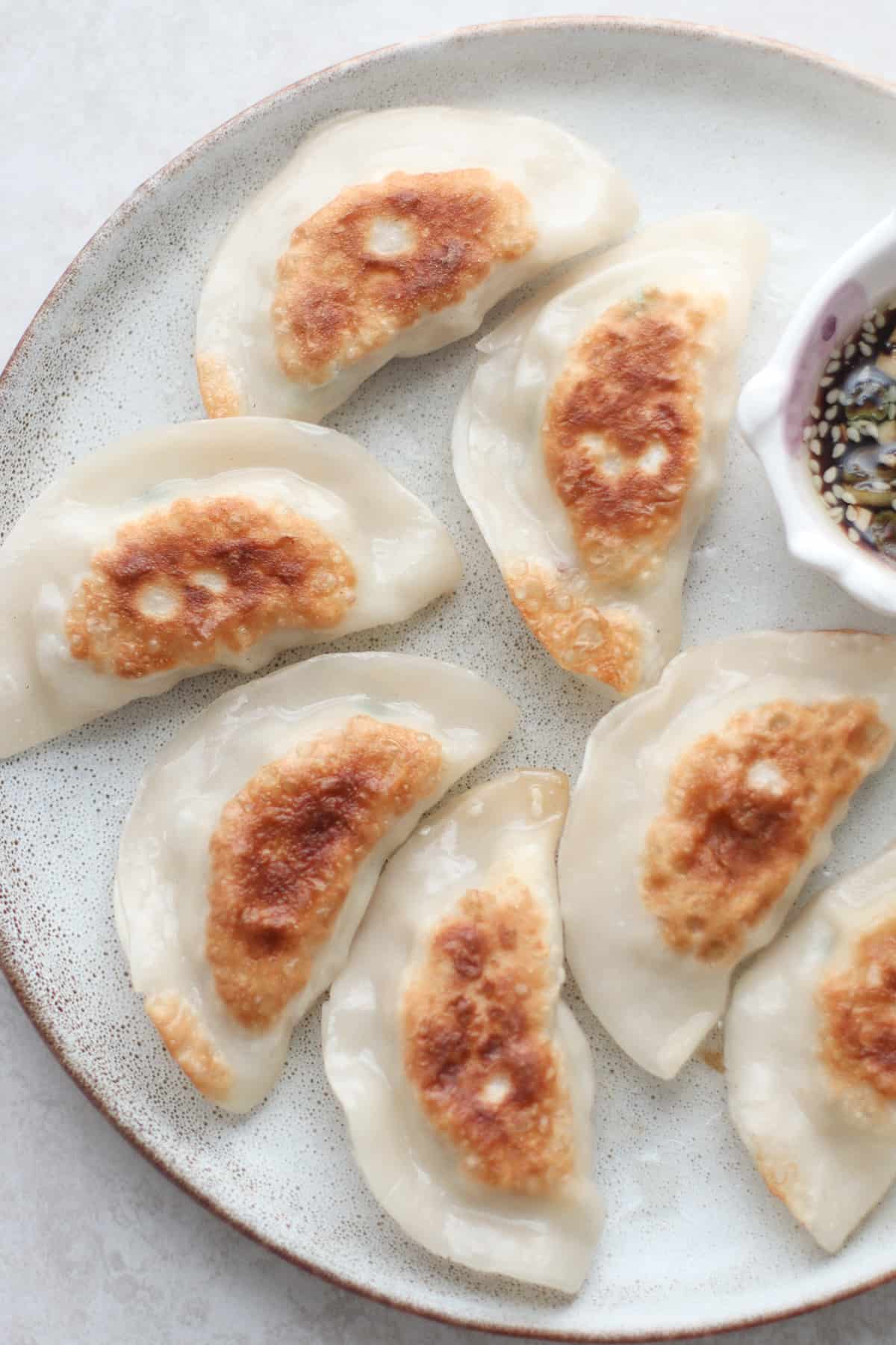 pan fried dumplings on a plate with dipping sauce.