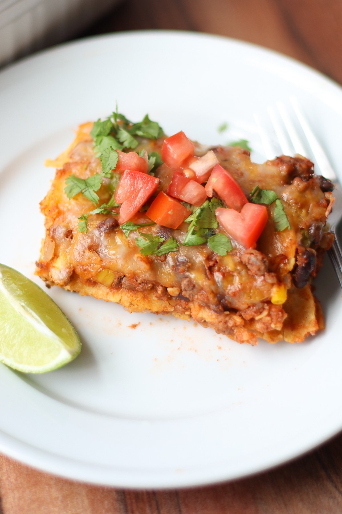 A big slice of enchilada casserole topped with tomatoes, cilantro.