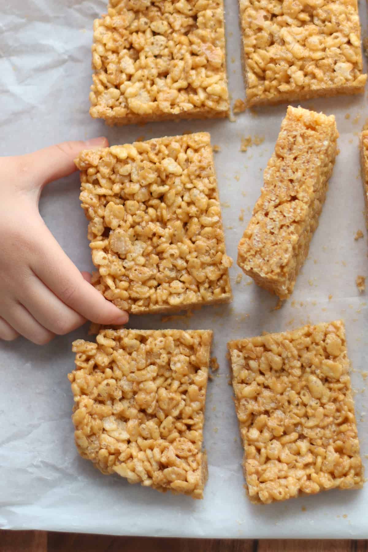 An overhead shot of sliced rice crispy treats with toddler's hand.