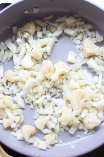 Cauliflower and chopped onions in a skillet.