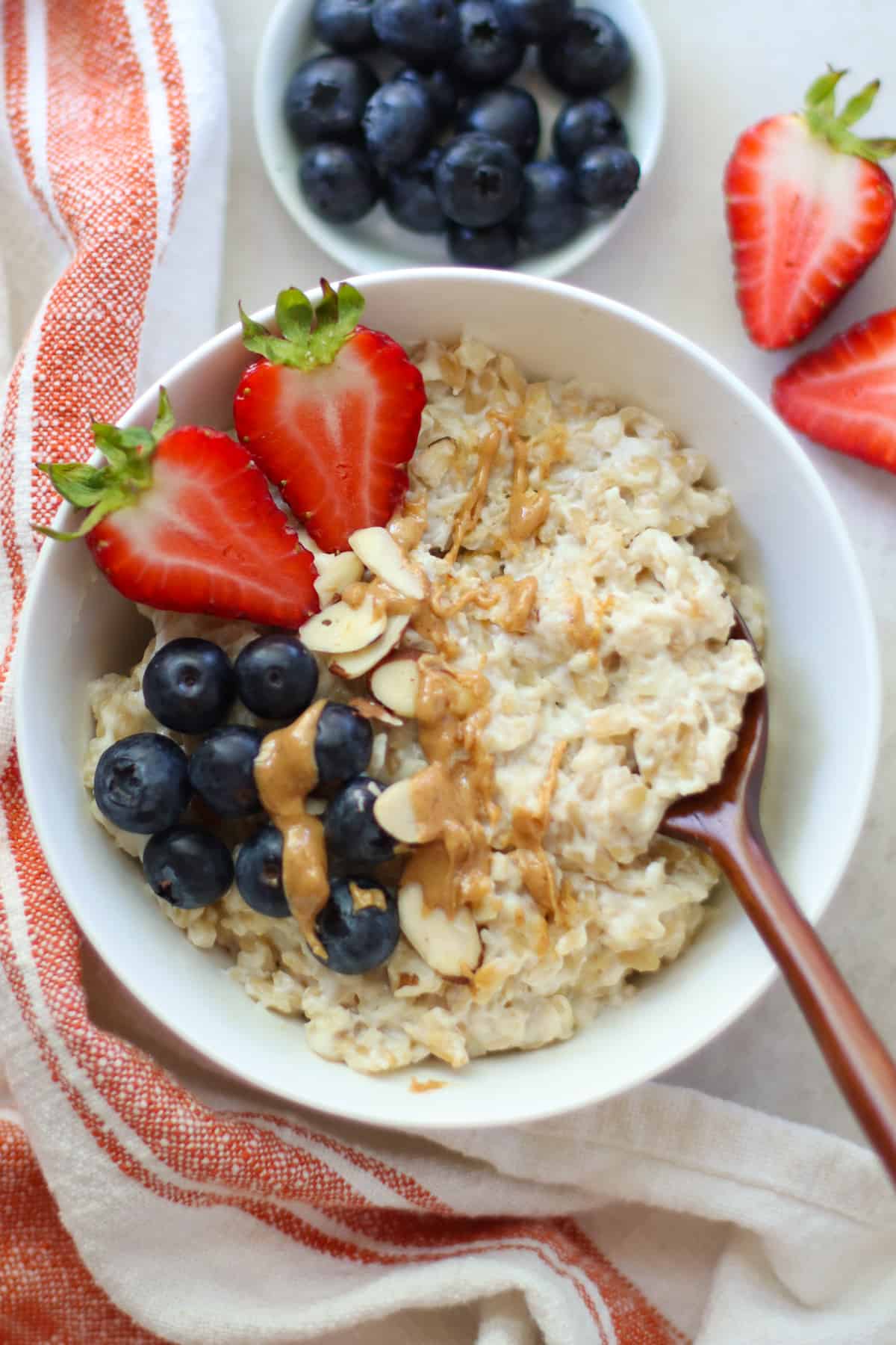 A bowl of oat pudding with strawberries, blueberries, and peanut butter.