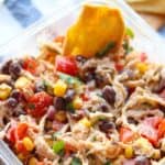 Close up of finished southwest chicken salad in a meal prep container with a tortilla chip in the top right corner of the container sitting on a blue and white striped dish towel.