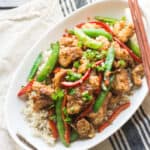 Mongolian chicken with snap peas and bell peppers in a large oval white dish with chopsticks