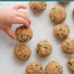 Baked salmon balls on parchment paper with toddler's hand grabbing one.