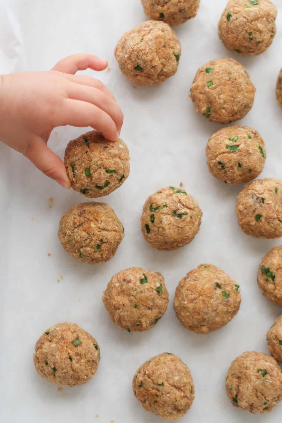 Baked salmon balls on parchment paper with toddler's hand grabbing one.