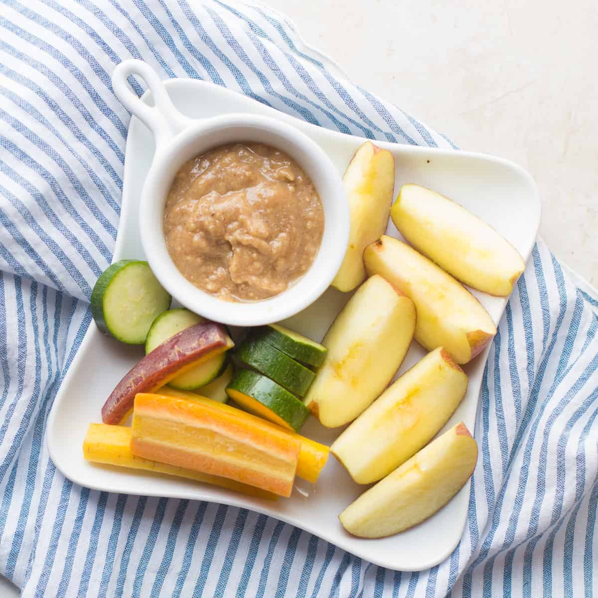 almond butter date syrup dip with sliced apples, carrots, and zucchini.