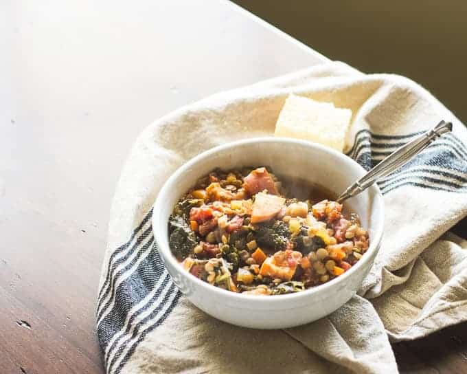 Thanksgiving lentil soup in a white bowl with a spoon and a side of bread