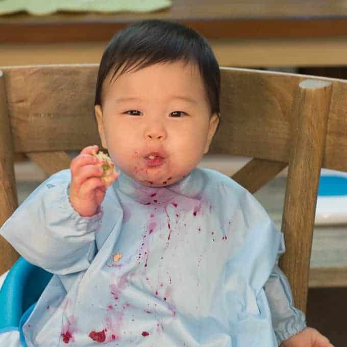 baby wearing a full-sleeved bib and eating beets.