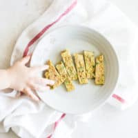 sliced egg veggie pancakes on a plate with a toddler hand reaching for one