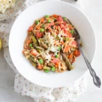 an adult portion of cooked orzo primavera on a white plate with shredded cheese and a fork