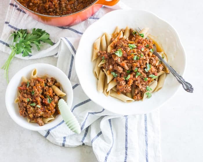 meat sauce over pasta on a large white bowl and a small portion for baby