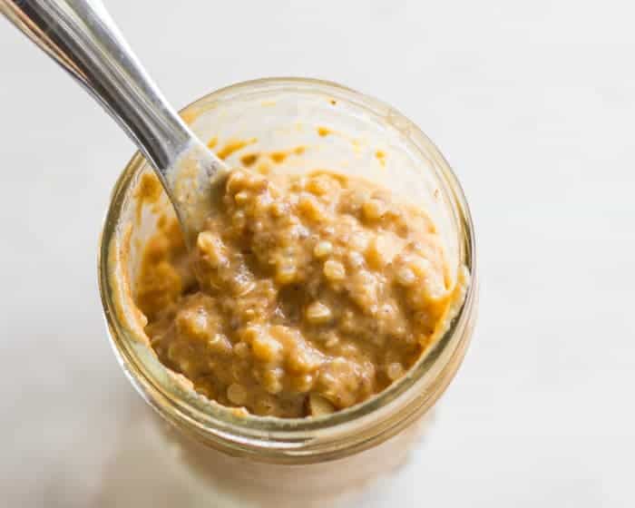 a close up shot of pumpkin pie overnight oats in a mason jar with a spoon