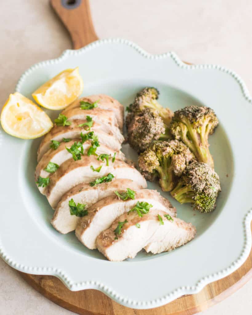 sliced chicken breast with a side of broccoli and squeezed lemon slices on a blue plate