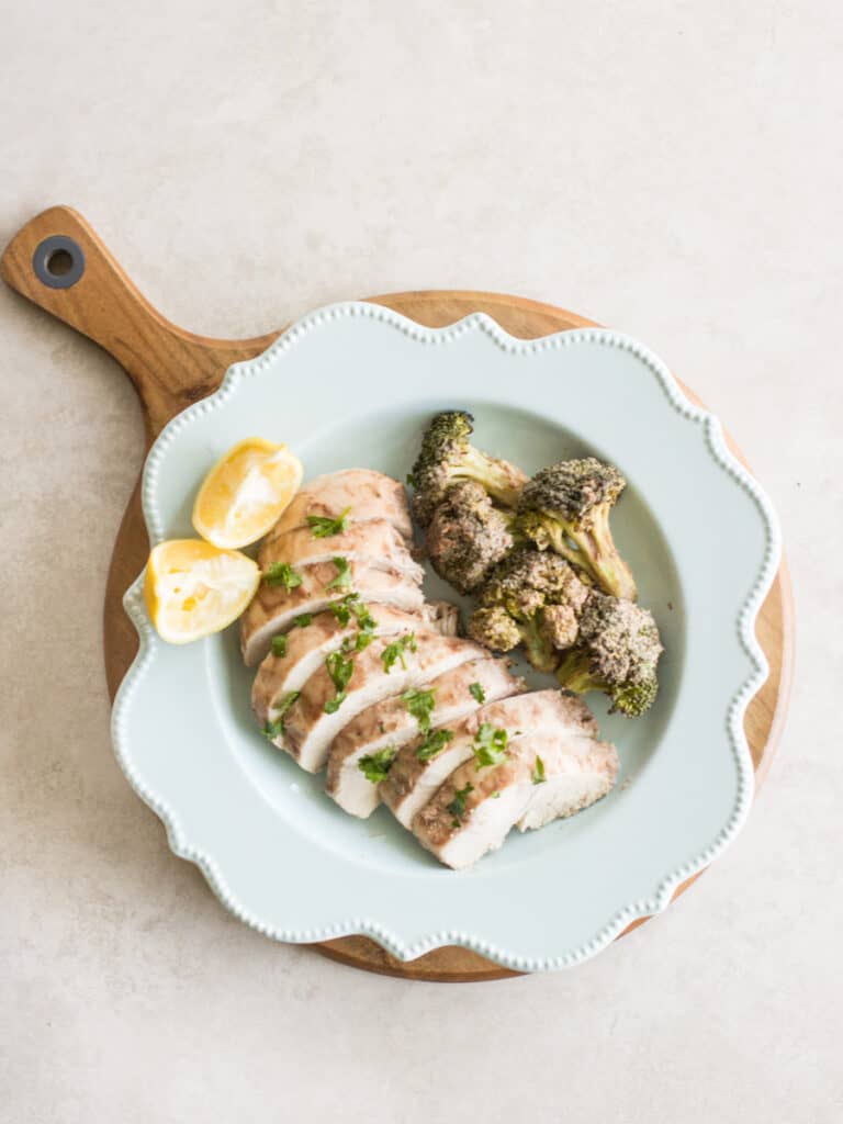 sliced chicken breast with a side of broccoli and squeezed lemon slices on a blue plate