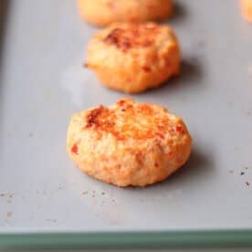 Baked shrimp cakes lines up on a large baking sheet.