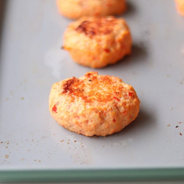 Baked shrimp cakes lines up on a large baking sheet.