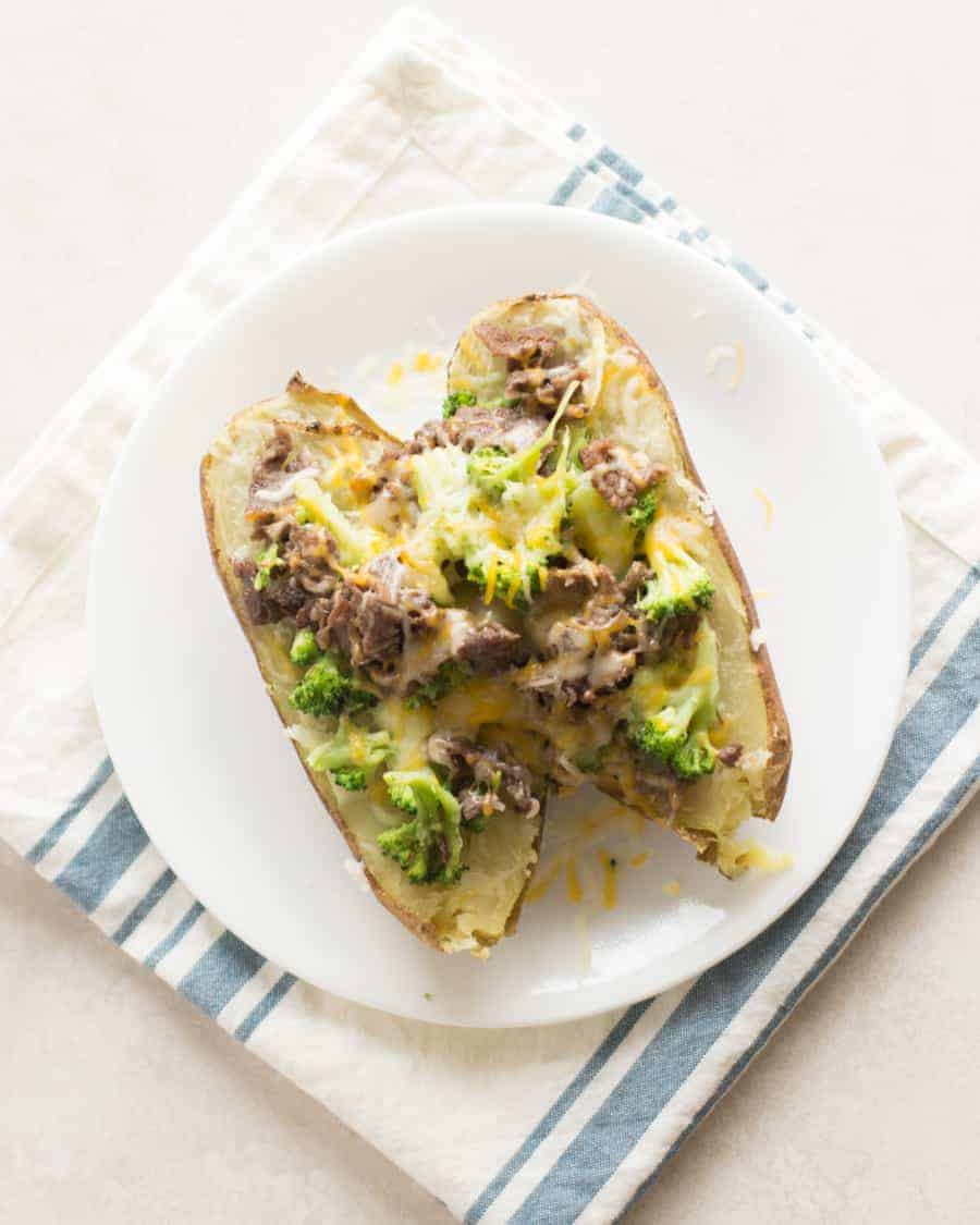 a large baked potatoes with meat, broccoli, and cheese served on a plate laid on top of folded kitchen towel