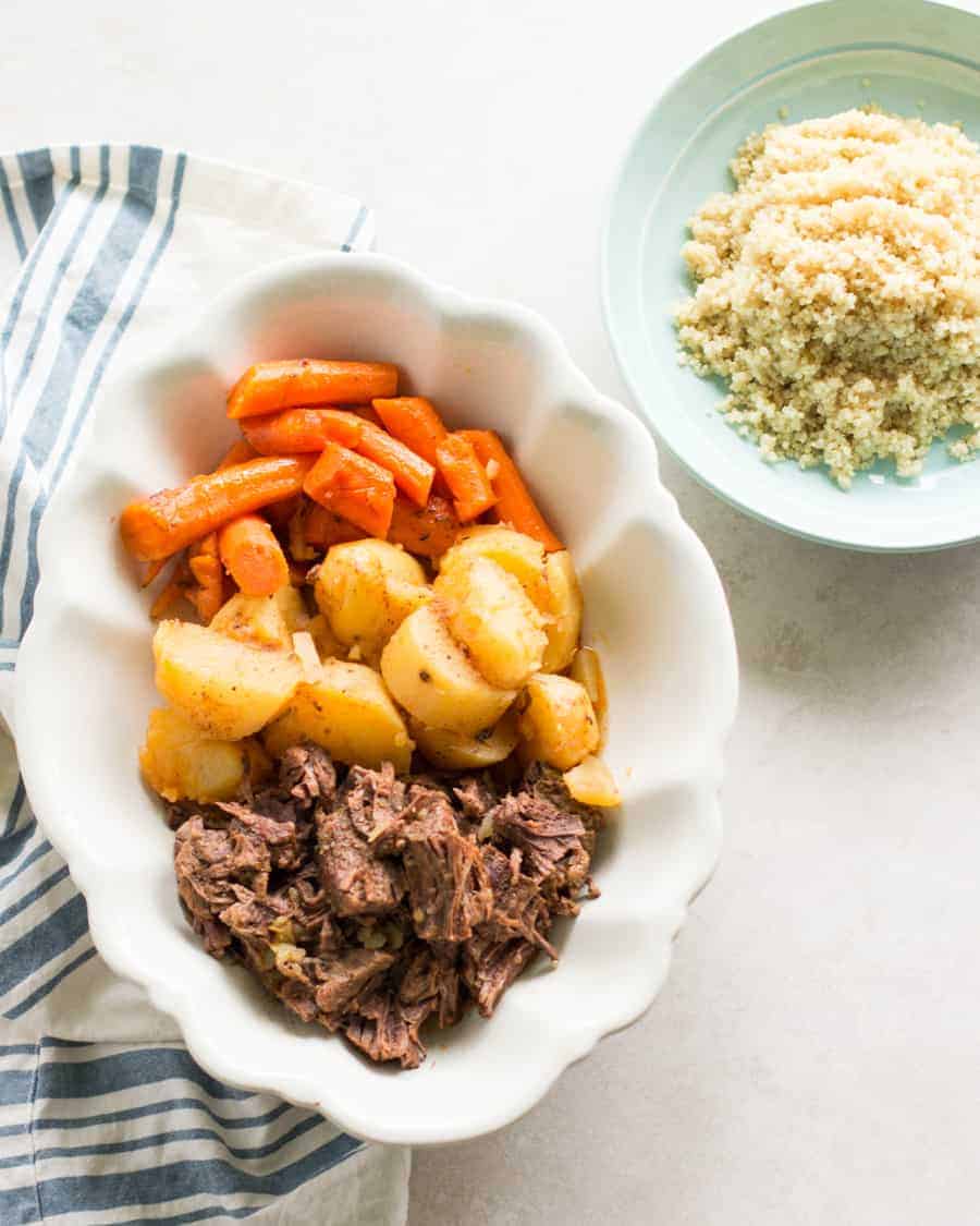 beef roast with potatoes and carrots served on a large white plate with quinoa on the side