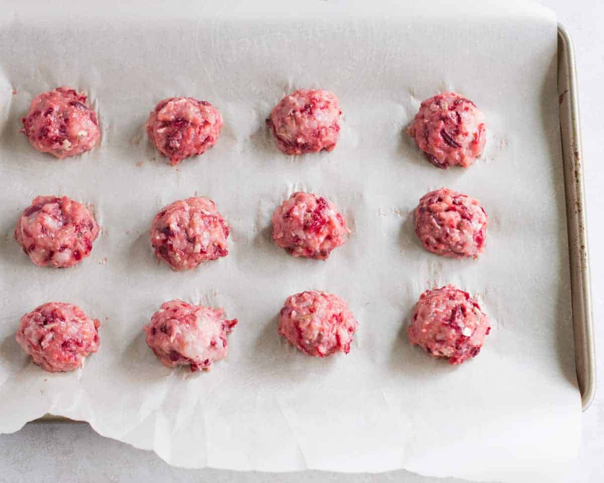 uncooked shape turkey beet meatballs on a baking tray lined with parchment paper