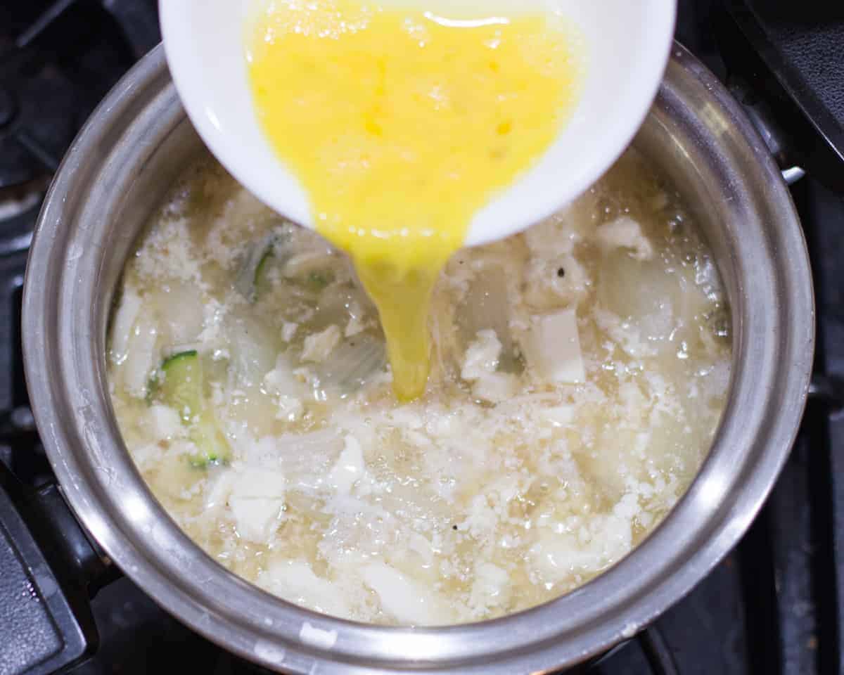 a whisked egg being added to the tofu soup