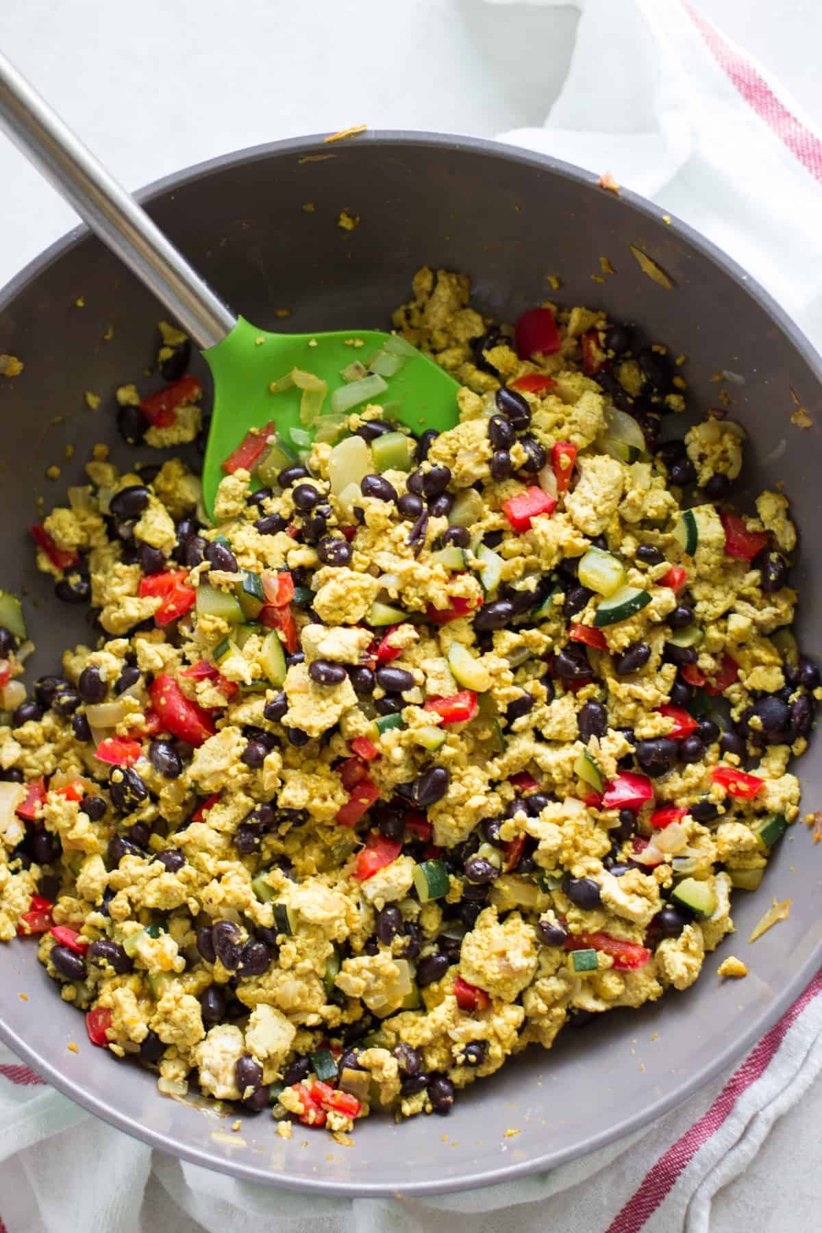 cooked veggie scramble in a skillet with green tipped spatula