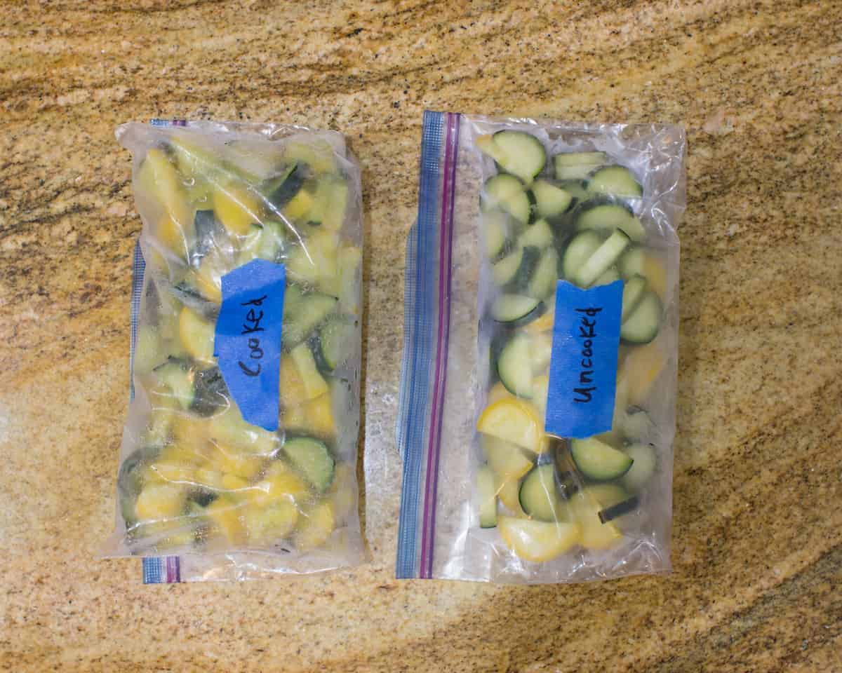two freezer safe bags with zucchini with blue masking tape labeled cooked and uncooked