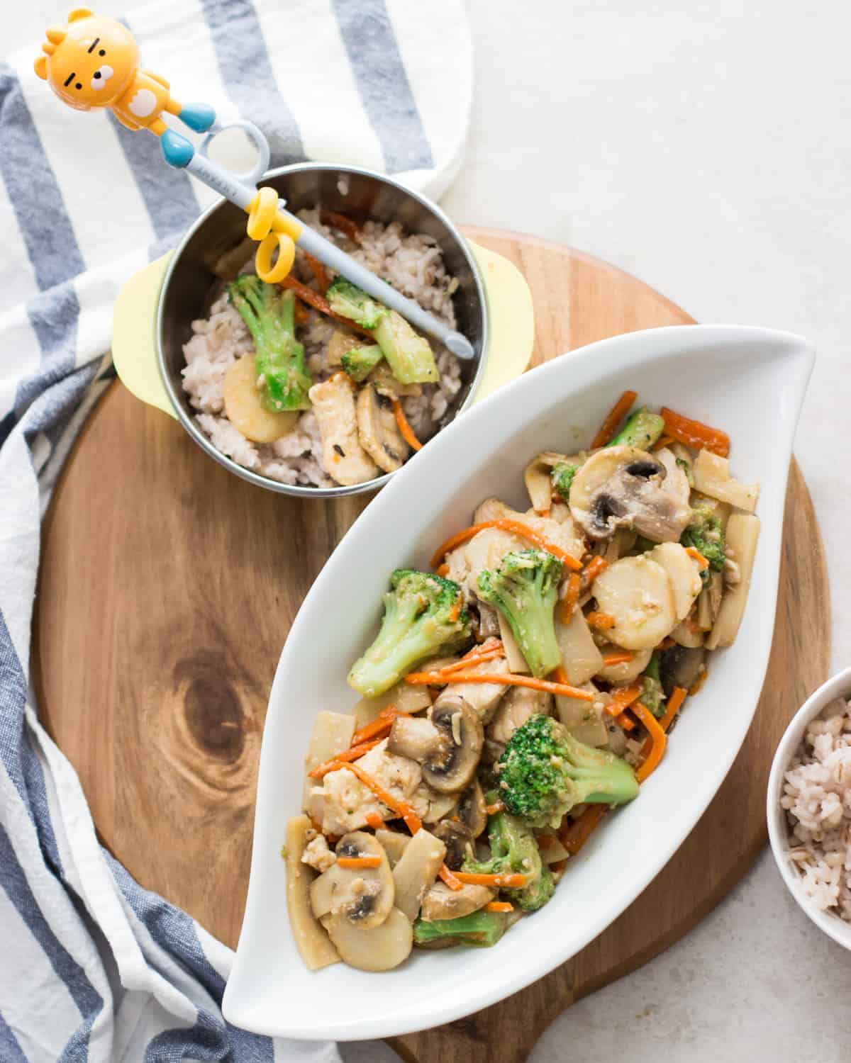 Chinese mushroom chicken plated on a large oval white dish and a bowl with rice and a small amount of the stir fry with chopsticks