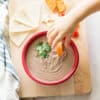 yogurt black bean dip in a large red bowl with a toddler hand dunking a sliced sweet potato