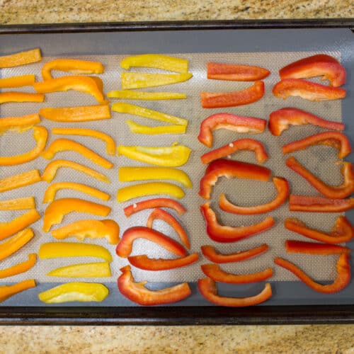showing how to freeze fresh peppers - orange yellow and red peppers spread out on a lined baking sheet