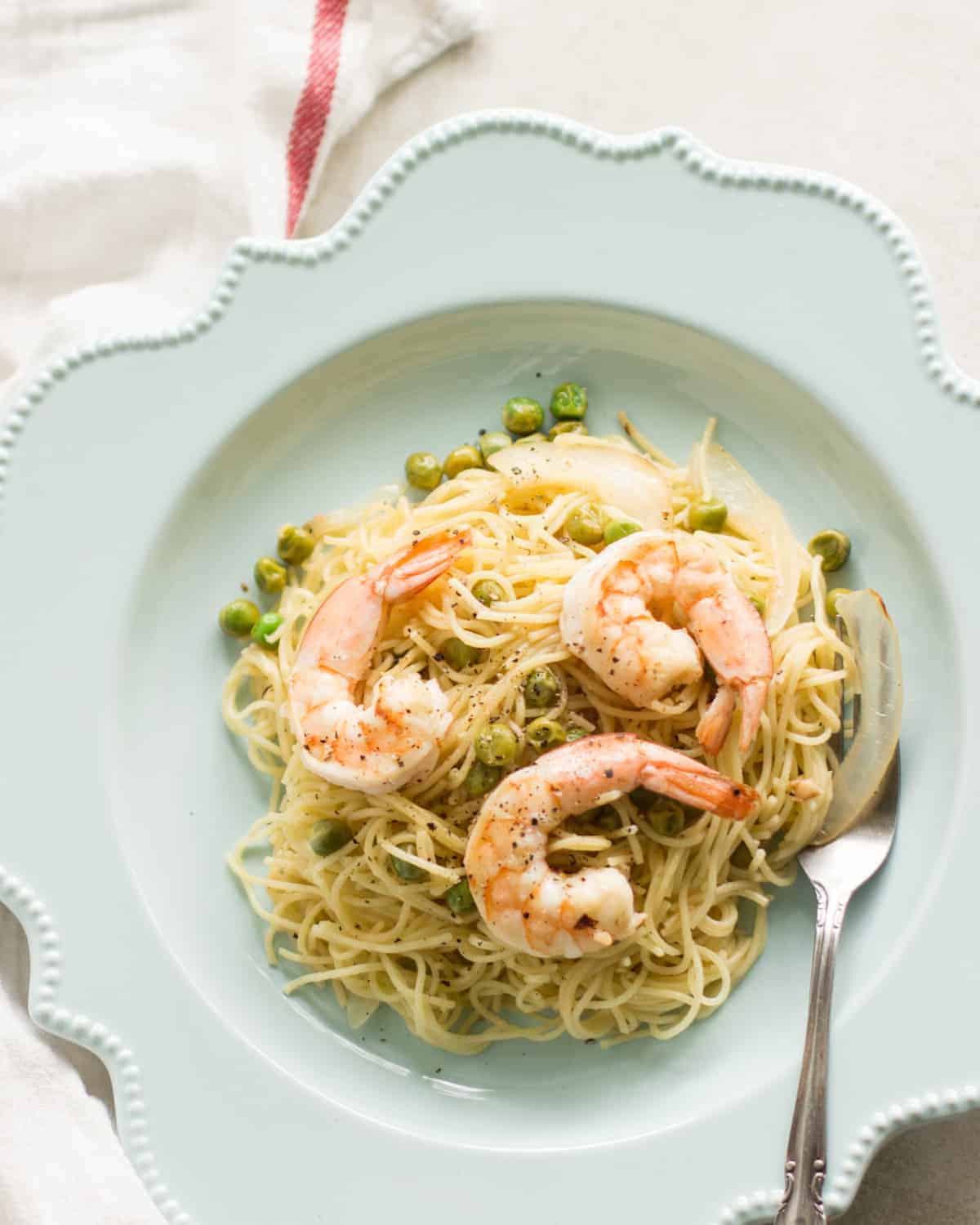 Shrimp scampi with peas served in a light blue plate with a fork