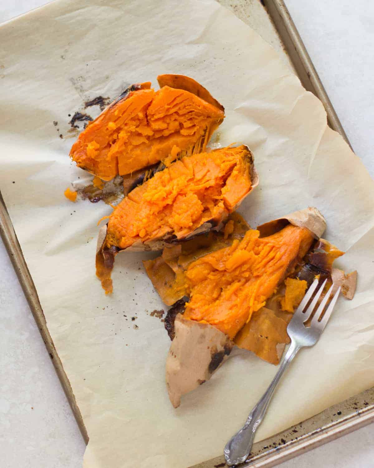 roasted orange sweet potatoes on a baking sheet with parchment paper