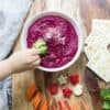 beetroot dip in a large white bowl with a toddler's hand dipping broccoli