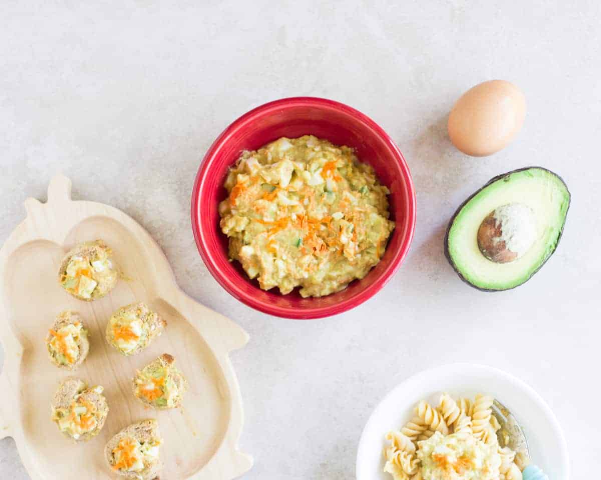 curried avocado egg salad in a red bowl with avocado and egg on the right
