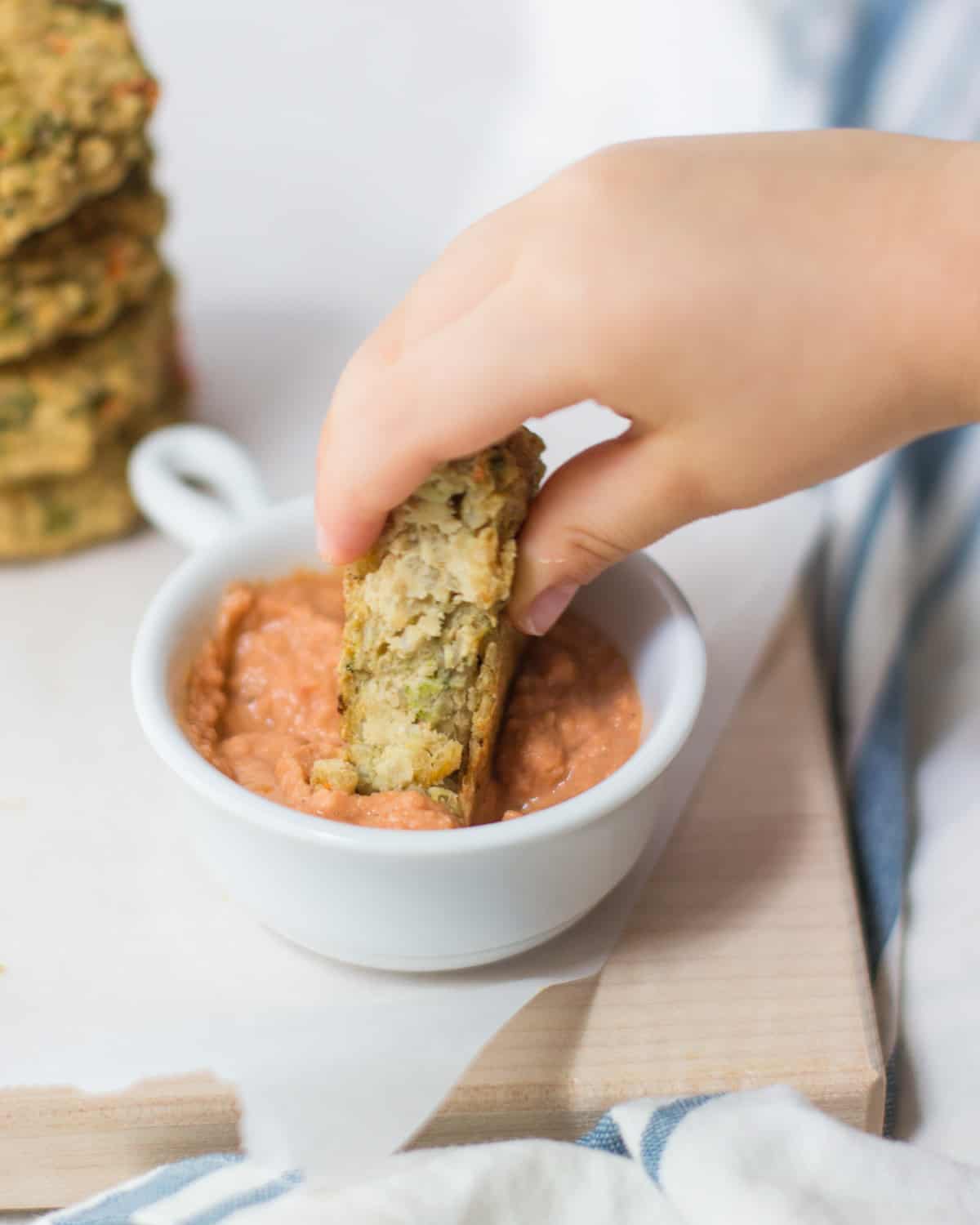 a toddler's hand dunking the chickpea cakes in pizza hummus