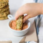 a toddler's hand dunking the chickpea cakes in pizza hummus