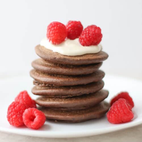 Stacked pancakes topped with yogurt and raspberries.