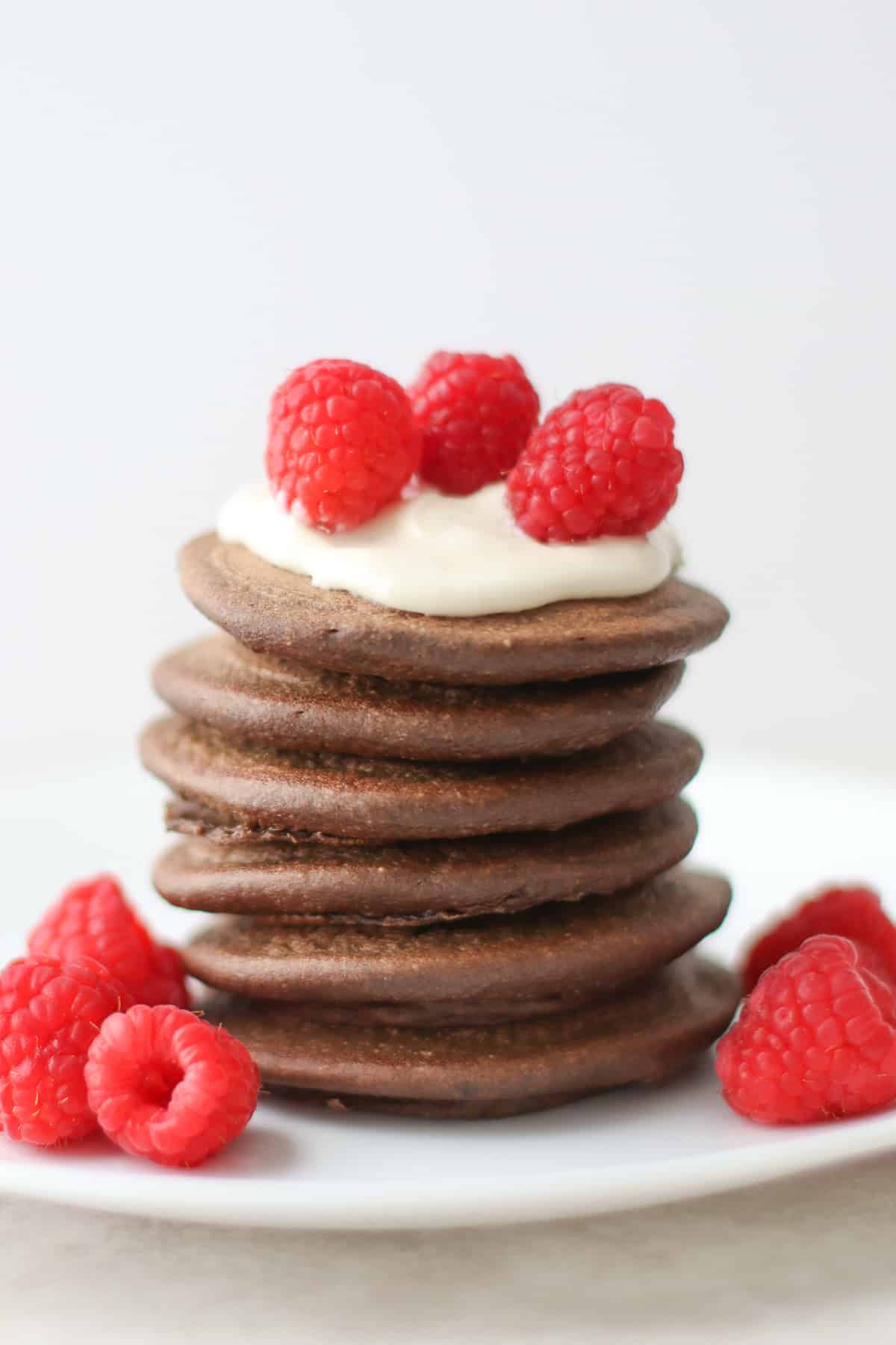 Stacked  pancakes topped with yogurt and raspberries.