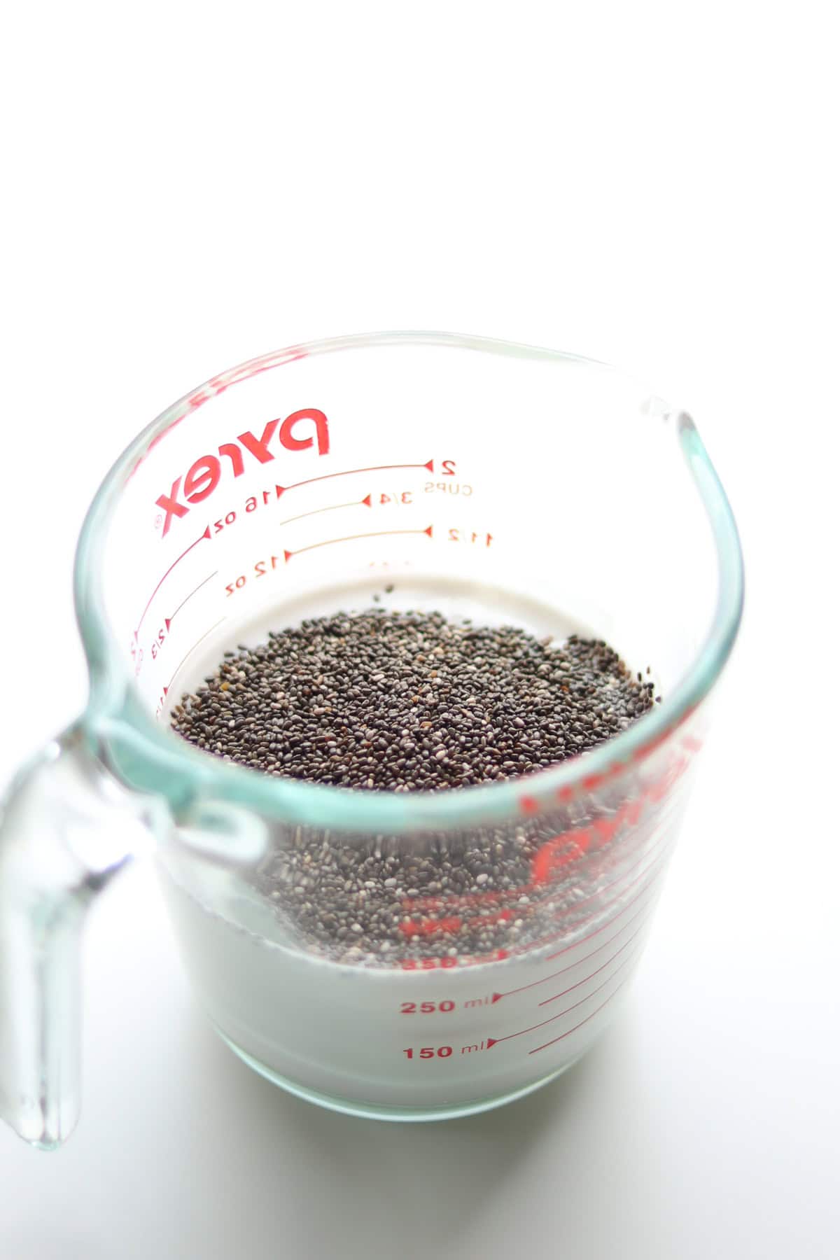Chia seed added to milk in a glass liquid measuring cup.