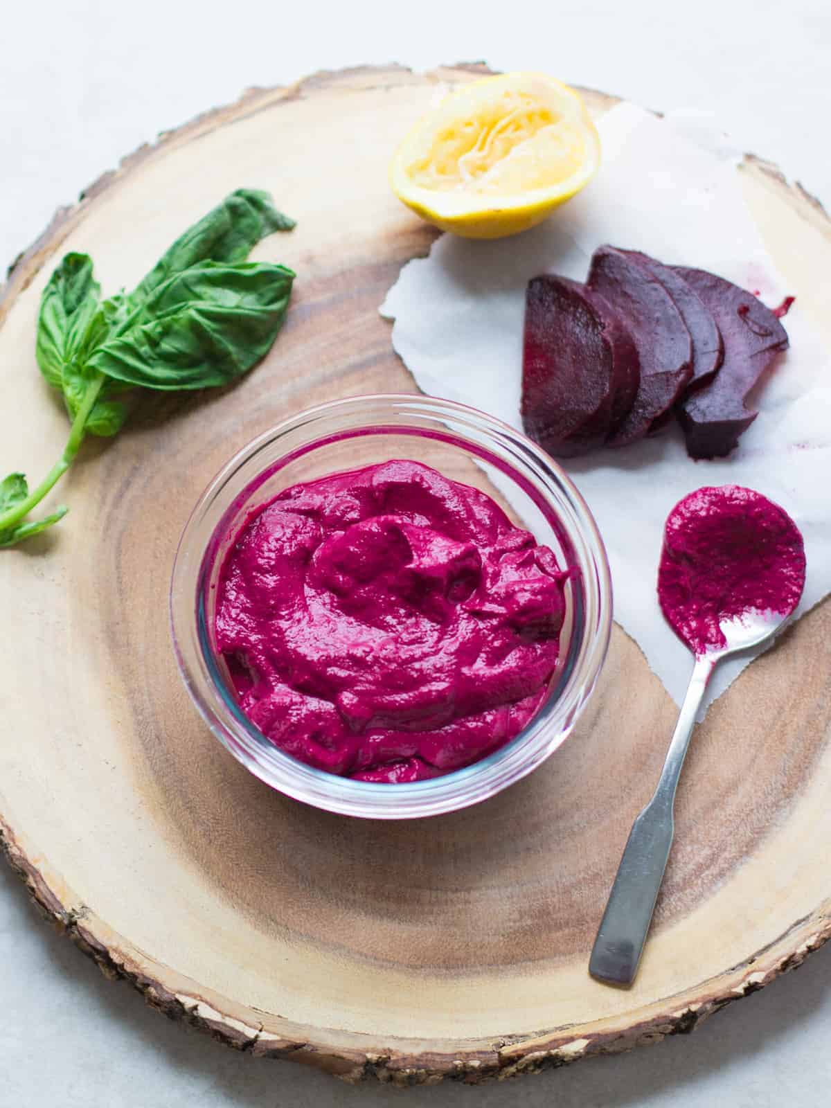 beetroot pesto in a glass bowl and placed on top of wooden round plate with other basil, beets, and lemon