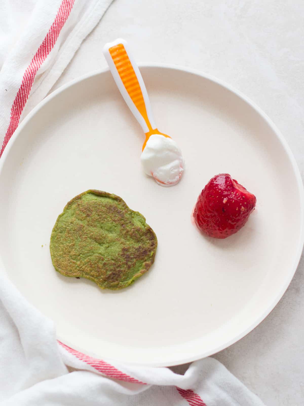 Baby's plate with one pancake, strawberry, yogurt.