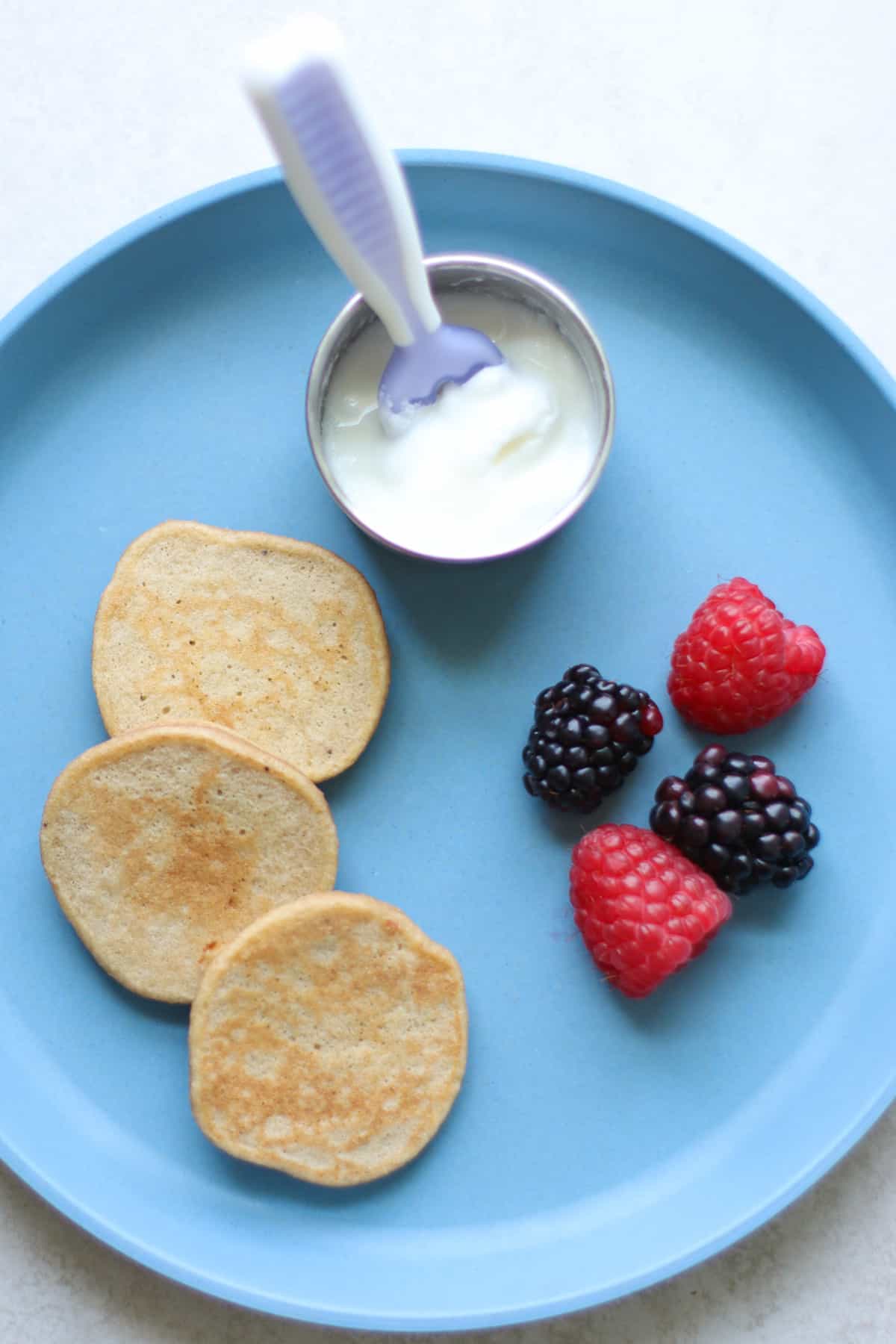 Three banana oat pancakes with yogurt and berries on baby's plate.