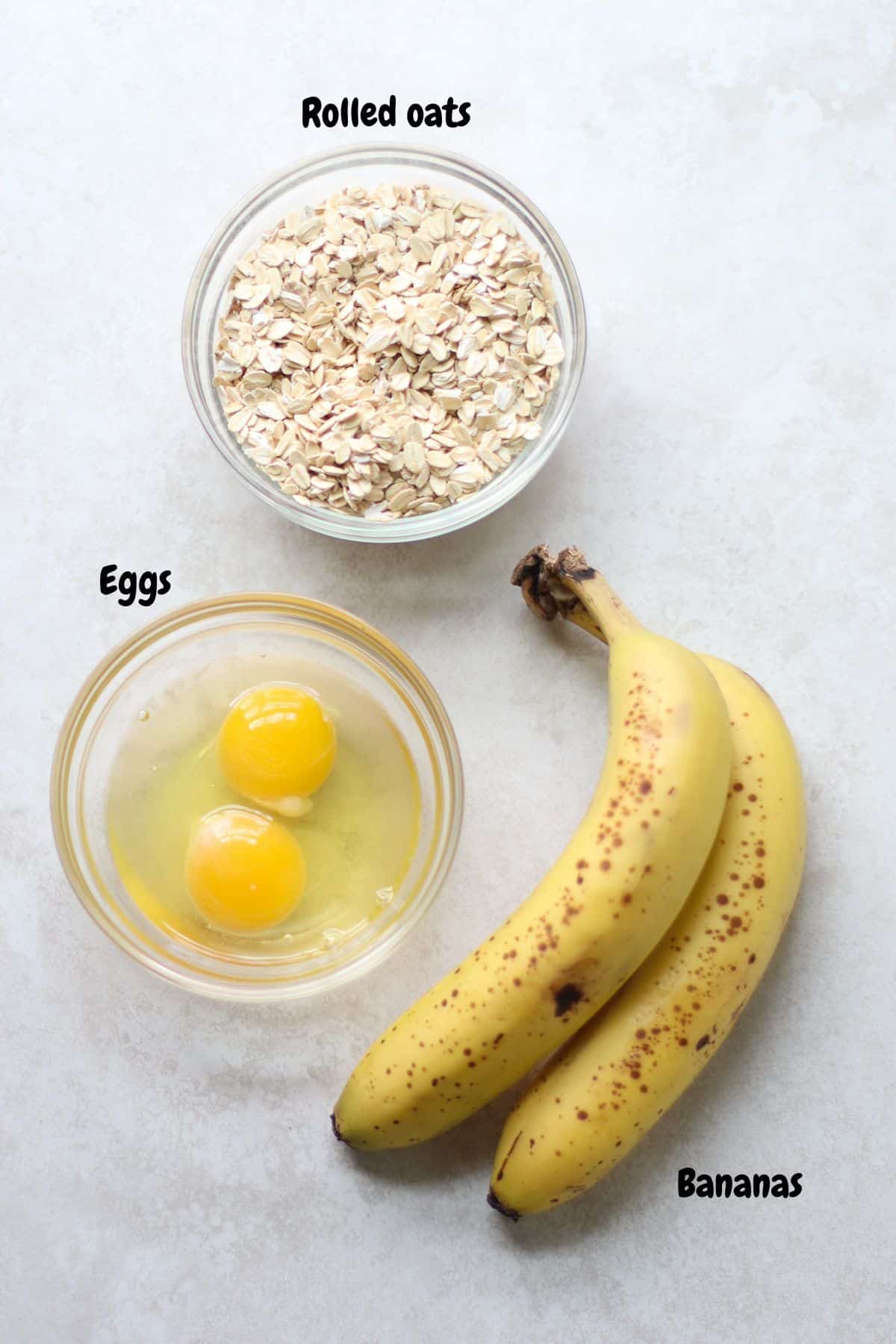 All the ingredients to make banana oat pancakes laid out on a white background.