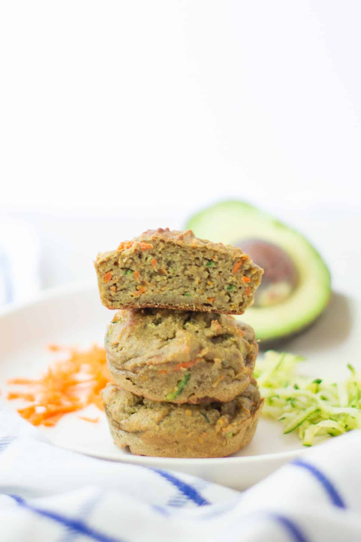 three stacked zucchini carrot avocado muffins with the very top one sliced in half to show the inside