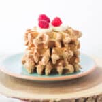 three stacked peanut butter waffles topped with banana and raspberries