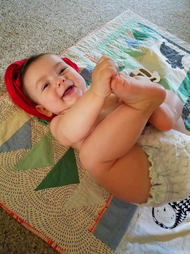 baby lying down on a blanket grabbing feet with his hands