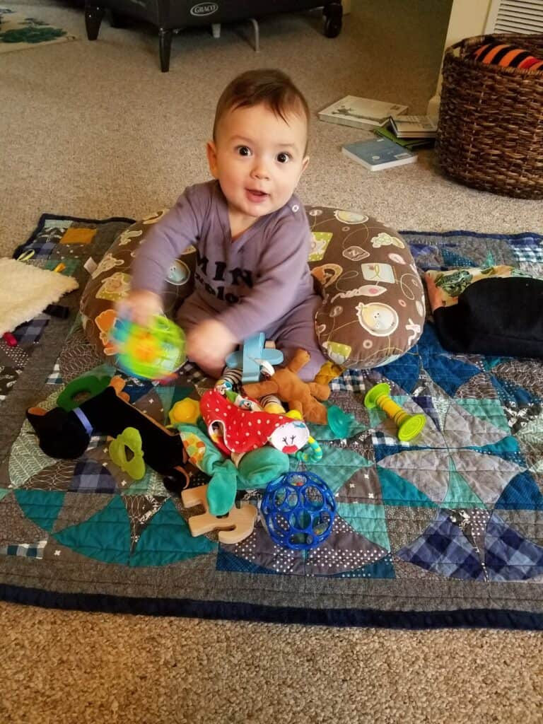 baby sitting up with boppy pillow behind and a bunch of toys in front to play with