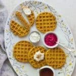 healthy pumpkin baby waffles on a fall decorative plate with ricotta, maple syrup, and beet dip in separate bowls