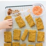 sliced pumpkin oatmeal bars on cooling rack with lentils and chopped pecans with toddler's hand reaching for one piece